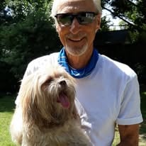 A man wearing sunglasses holding a small dog outdoors